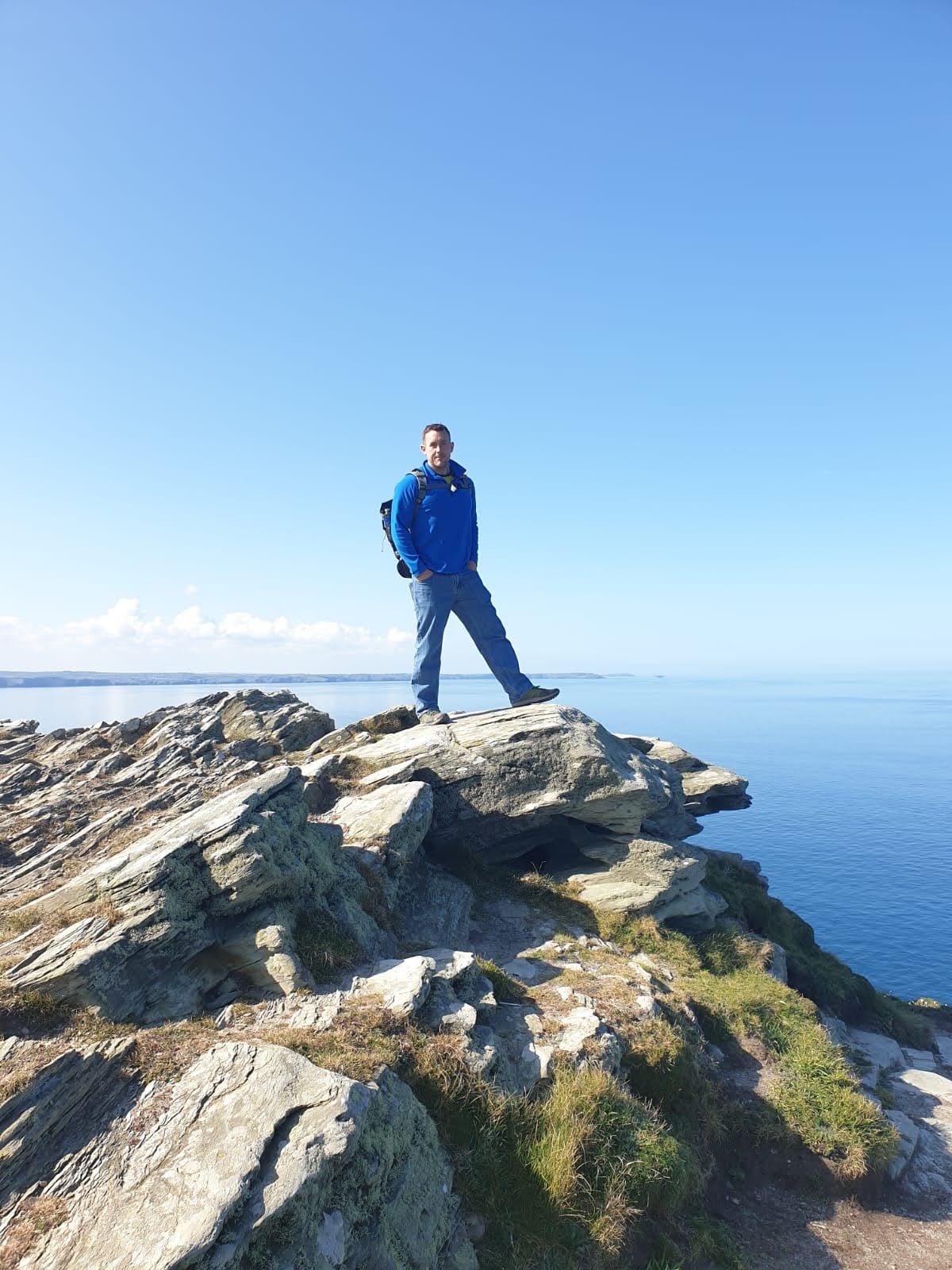 Roger standing on a cliff edge above a calm sea, the moment before action