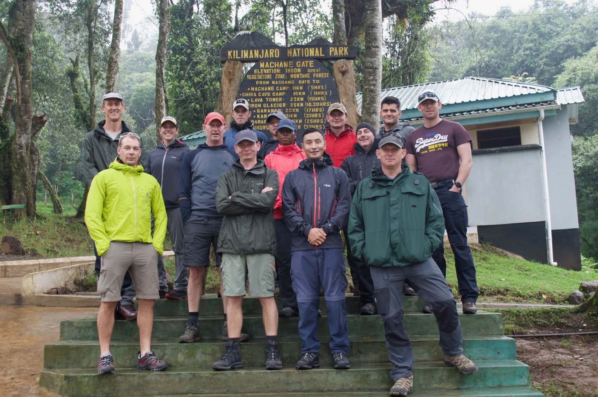 Team of fourteen trekkers and leaders gathered at the Machame Gate sign, ready to begin the Kilimanjaro expedition.